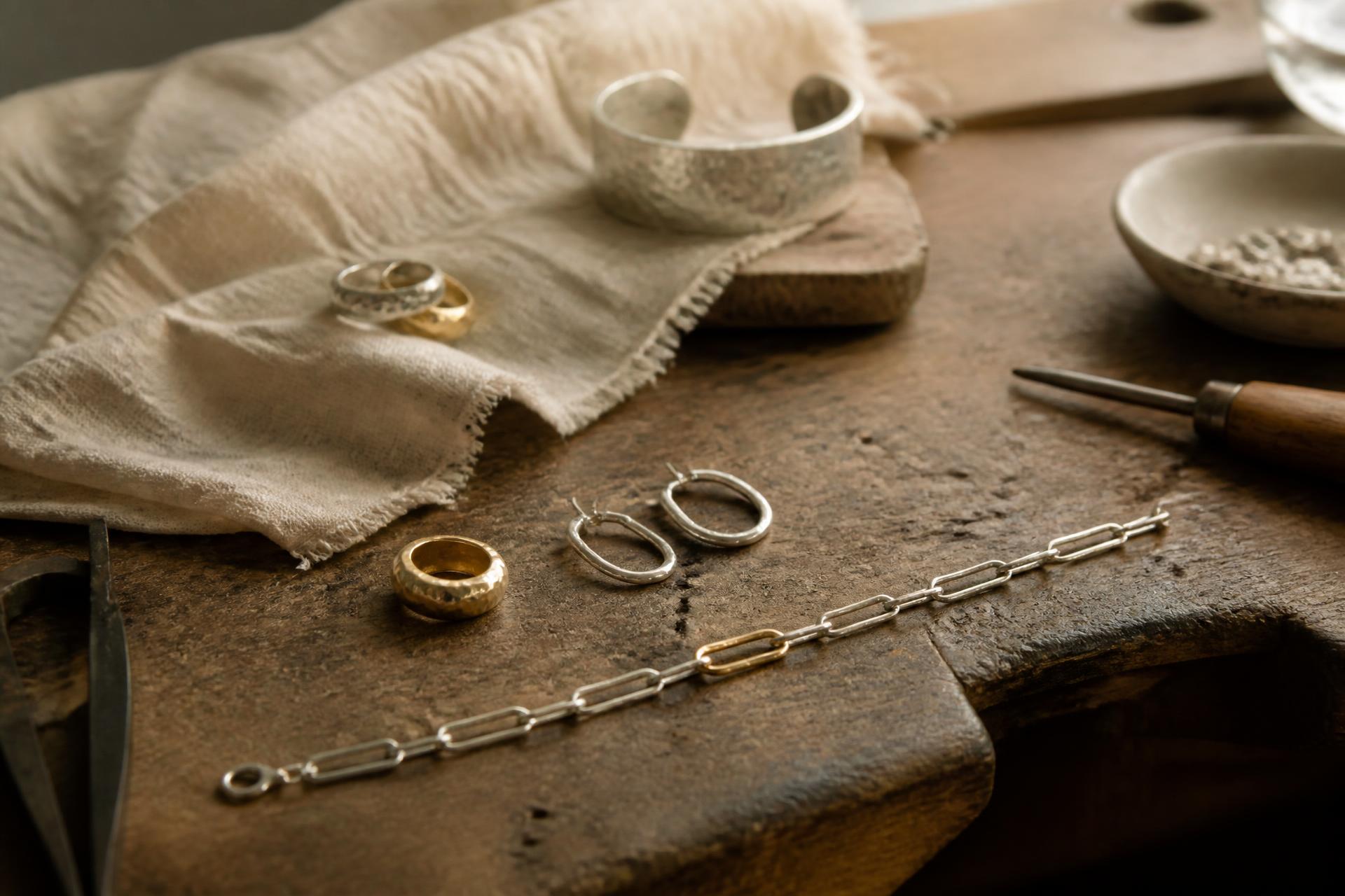 Handmade silver and gold rings, hoops and a chain bracelet resting on a worn workshop bench